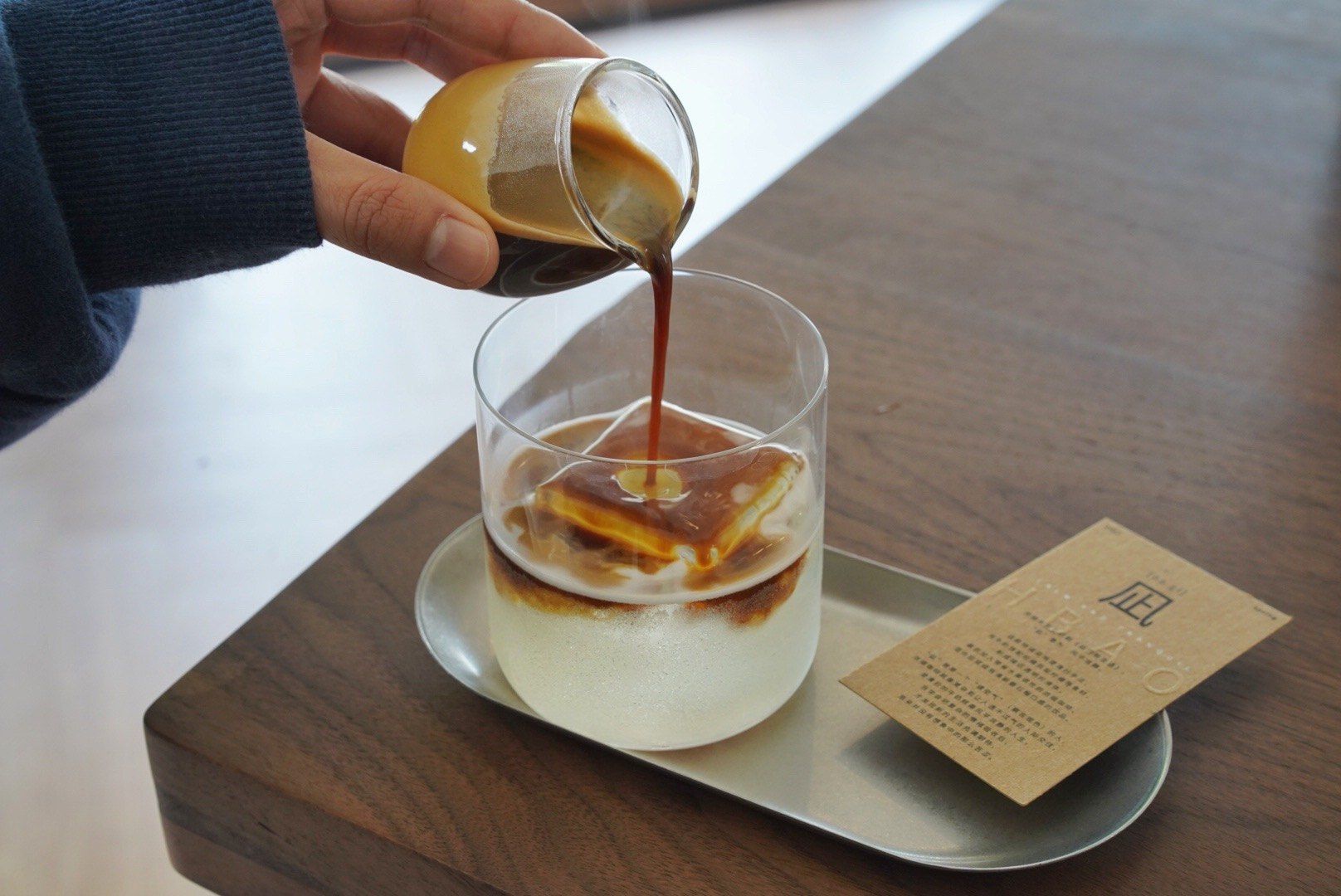 正在将咖啡从小玻璃杯倒入装有冰块的饮品杯